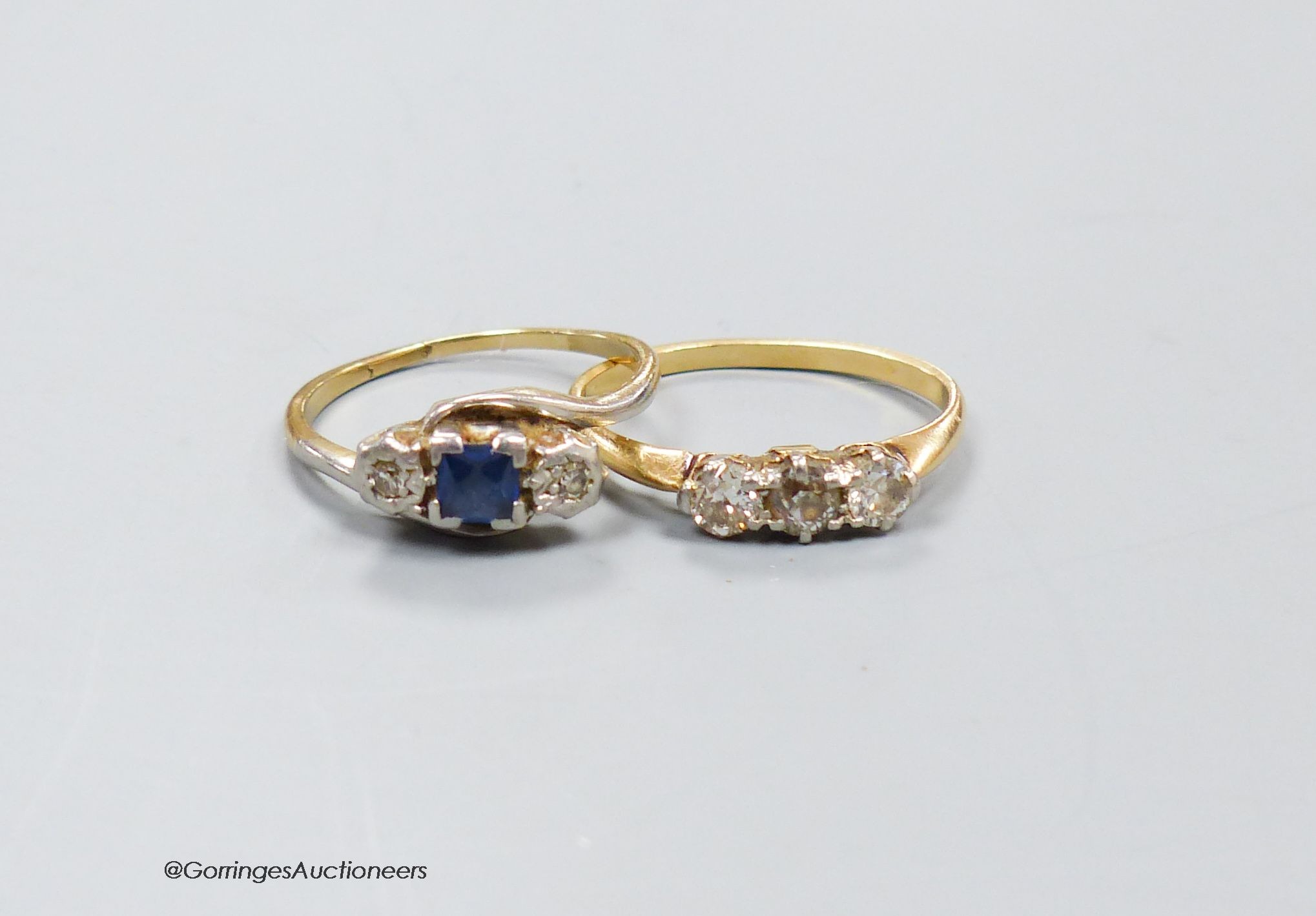 A three stone diamond ring, size M, 2.4g, and a three stone diamond and sapphire ring, size O, 2.5g.